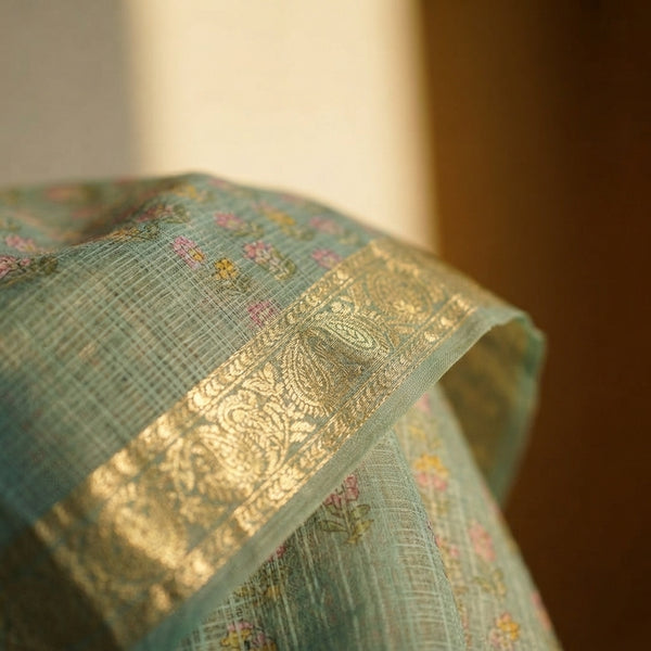 Close-up of a sea green handblock printed saree featuring an intricate golden zari border on breathable fabric.